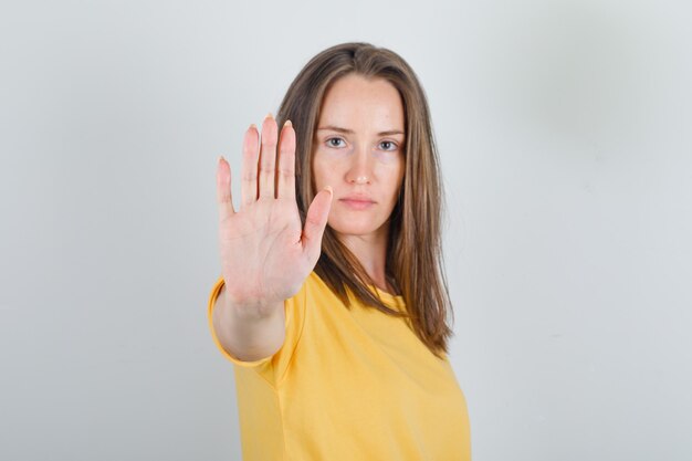 Mujer joven mostrando suficiente gesto con la mano en camiseta amarilla y mirando fatigado