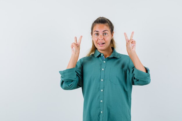 Mujer joven mostrando V-sign en camisa azul y mirando alegre