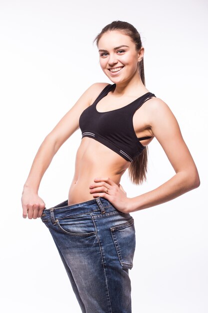 Mujer joven muestra su pérdida de peso usando unos jeans viejos
