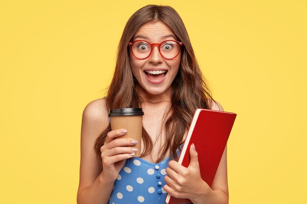 Mujer joven muy alegre con gafas posando contra la pared amarilla