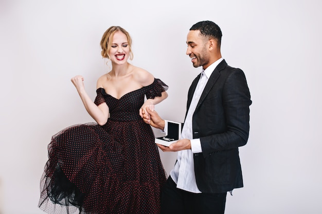 Mujer joven muy emocionada en vestido de lujo que expresa emociones felices brillantes cerca de chico guapo con regalo. Gran regalo, sonriente, felicidad, San Valentín, amantes.