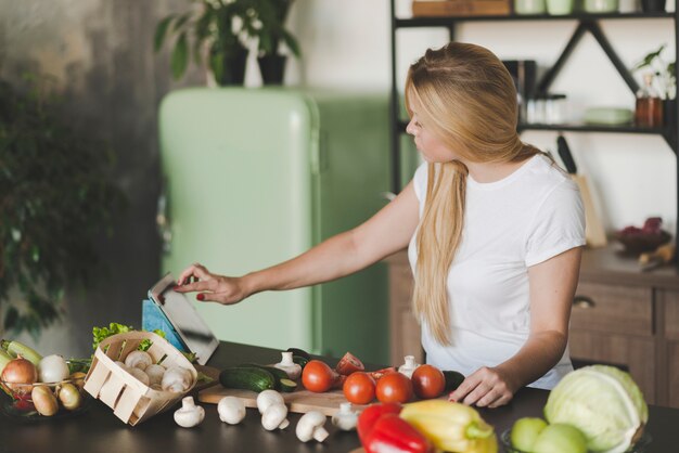 Mujer joven navegando en tableta digital mientras se prepara la comida