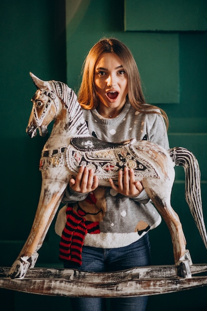 Foto gratuita mujer joven en navidad con silla de pony de madera