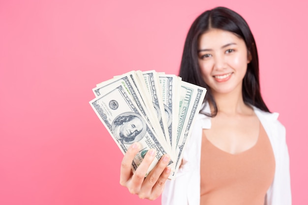 Mujer joven del negocio asiático hermoso acertado que lleva a cabo cuentas del dólar de EE. UU. Del dinero disponibles en fondo rosado