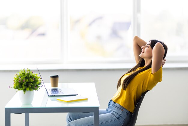 Mujer joven de negocios relajándose con las manos detrás de la cabeza y sonriendo