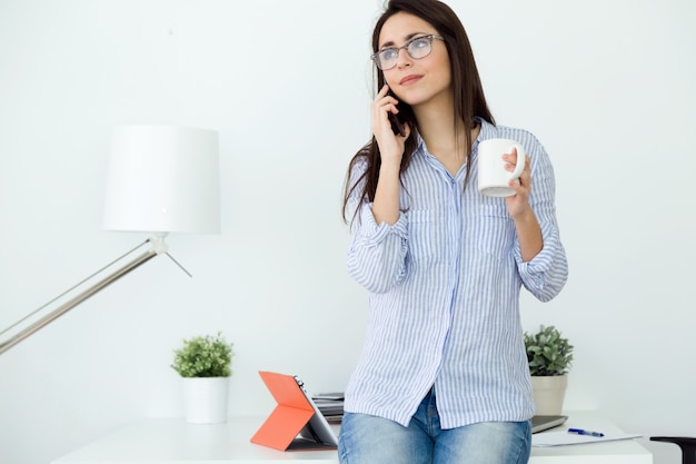 Mujer joven de negocios utilizando su teléfono móvil en la oficina.