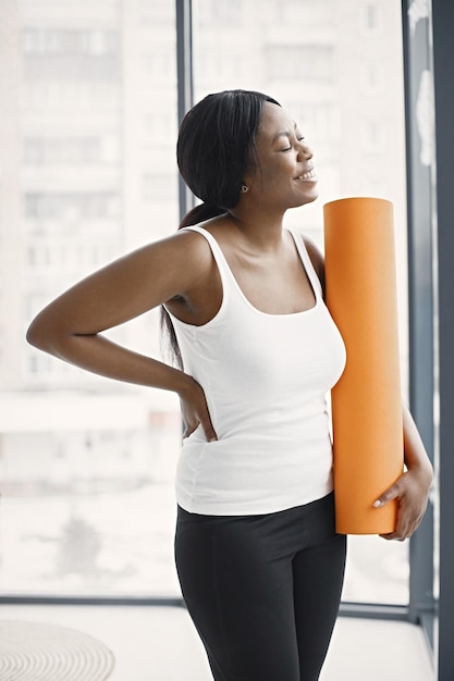 Mujer joven negra después del entrenamiento sosteniendo una alfombra de yoga naranja