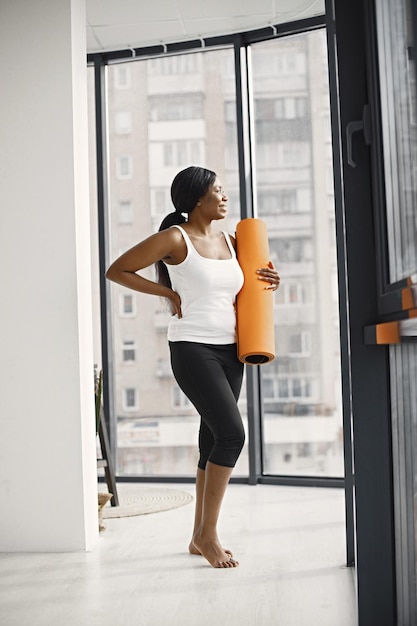 Mujer joven negra lista para hacer ejercicio sosteniendo una alfombra de yoga naranja