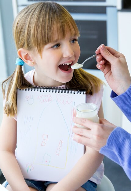 Una mujer joven y niña comiendo yogur en la cocina