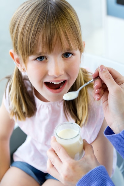 Una mujer joven y niña comiendo yogur en la cocina