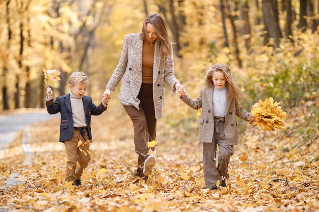 Mujer joven y niña y niño caminando en el bosque de otoño. Mujer, su hija y su hijo jugando y divirtiéndose. Chica con traje gris de moda y chaqueta azul chico.