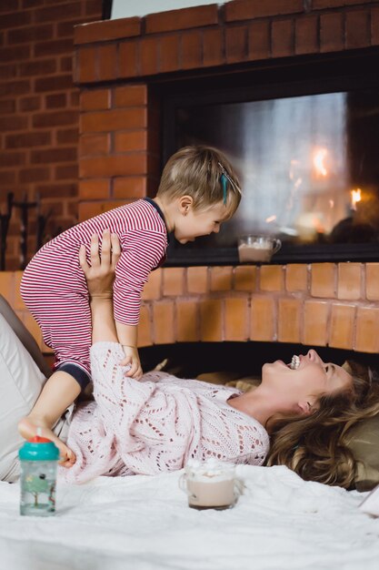 Mujer joven con un niño. Mamá e hijo están jugando, divirtiéndose cerca de la chimenea.