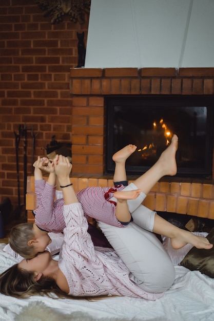 Mujer joven con un niño. Mamá e hijo están jugando, divirtiéndose cerca de la chimenea.