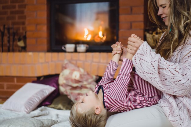 Mujer joven con un niño. Mamá e hijo están jugando, divirtiéndose cerca de la chimenea.