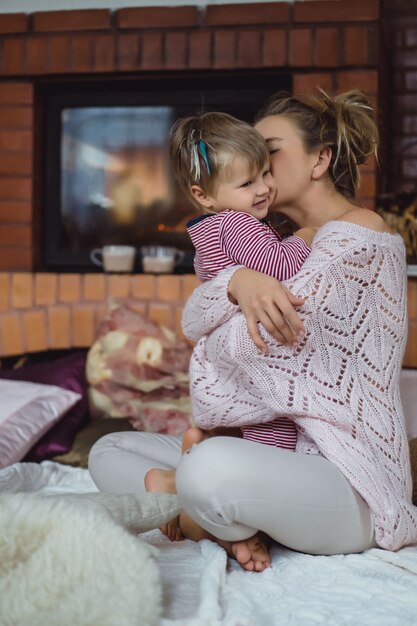 Mujer joven con un niño. Mamá e hijo están jugando, divirtiéndose cerca de la chimenea.