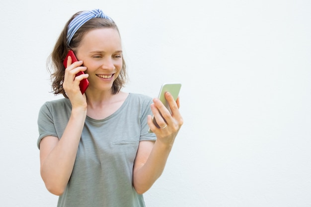 Mujer joven ocupada feliz que usa dos teléfonos móviles