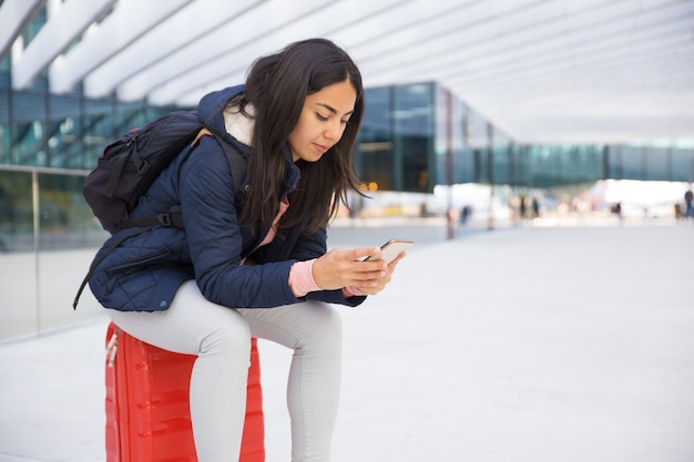 Mujer joven ocupada seria que usa smartphone en aeropuerto