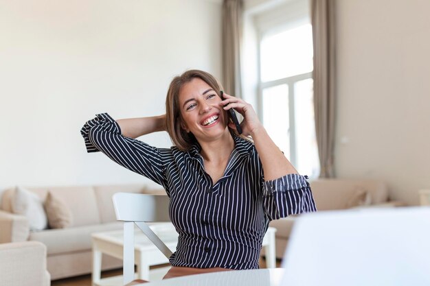 Mujer joven de oficina hablando con alguien en su teléfono móvil mientras mira a la distancia con expresión facial feliz