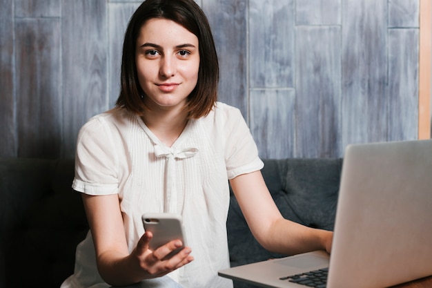 Mujer joven en la oficina con ordenador portátil y teléfono inteligente