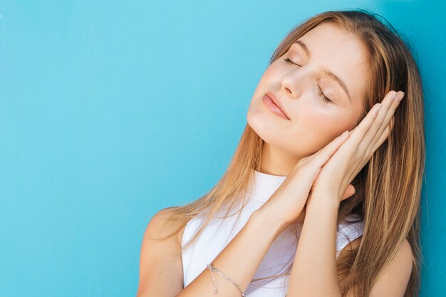 Mujer joven con el ojo cerrado durmiendo contra el fondo azul