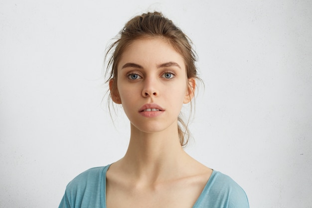 Mujer joven con ojos azules y cabello recogido que parece orgullosa y orgullosa de sí misma teniendo éxito durante las clases. Mujer caucásica con bello rostro mostrando su elegancia