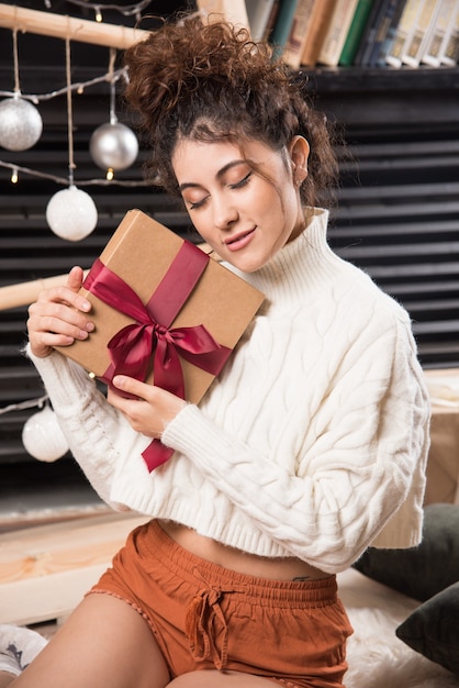 Una mujer joven con los ojos cerrados sosteniendo una caja de regalo con lazo