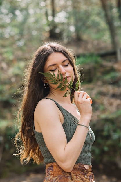 Foto gratuita mujer joven oliendo una hoja en el bosque