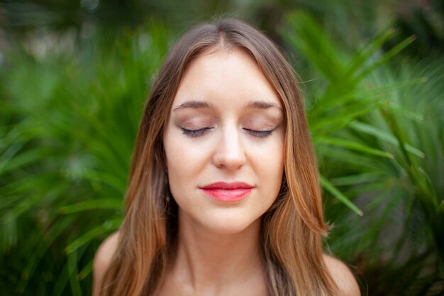 Mujer joven pacífica con los ojos cerrados disfrutando de sonidos de la naturaleza