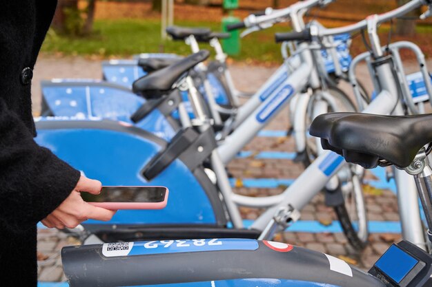 Mujer joven pagando por alquiler de bicicletas con smartphone