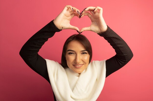 Mujer joven con pañuelo blanco haciendo gesto de corazón con los dedos sobre la cabeza sonriendo alegremente