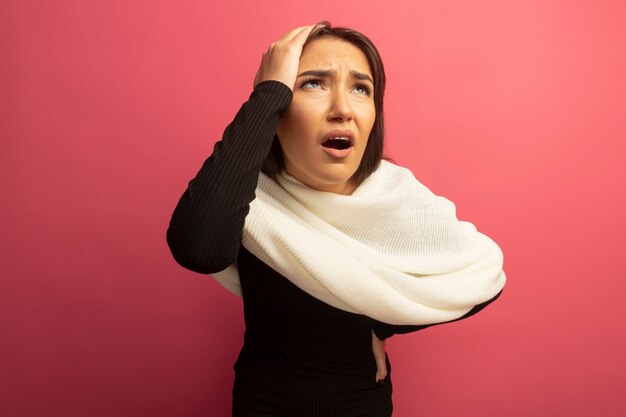 Mujer joven con pañuelo blanco mirando confundido con la mano en la cabeza.