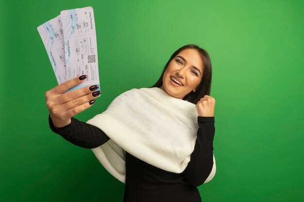 Mujer joven con pañuelo blanco mostrando billetes de avión feliz y alegre puño apretado regocijándose de su éxito