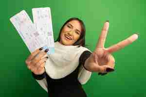 Foto gratuita mujer joven con pañuelo blanco mostrando billetes de avión sonriendo feliz y alegre mostrando v-sign