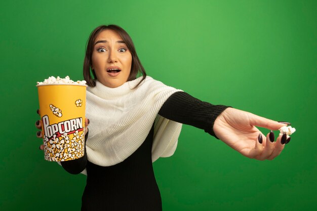 Mujer joven con pañuelo blanco mostrando cubo con palomitas de maíz confundido con el brazo extendido