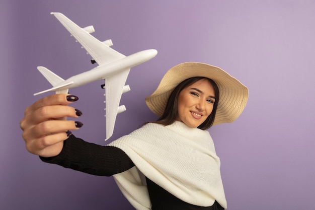 Mujer joven con pañuelo blanco en sombrero de verano mostrando avión de juguete sonriendo feliz y alegre