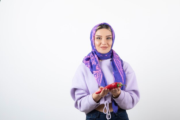 mujer joven en pañuelo sosteniendo un pimiento rojo.