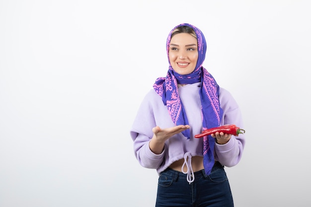 mujer joven en pañuelo sosteniendo un pimiento rojo.