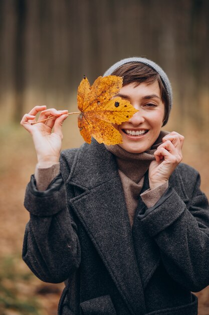 Mujer joven en el parque otoño sosteniendo la hoja por la cara