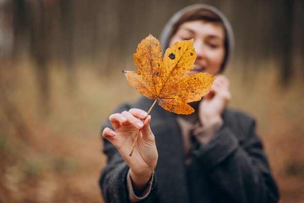 Mujer joven en el parque otoño sosteniendo la hoja por la cara