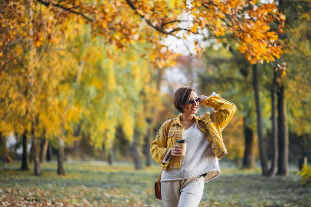 Mujer joven en un parque de otoño tomando café