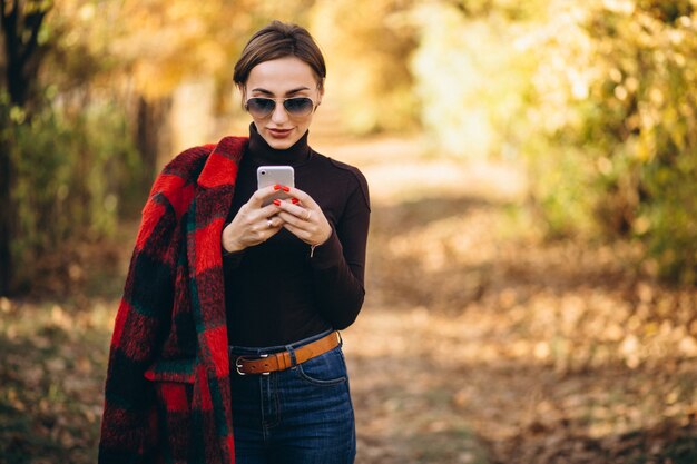 Mujer joven en el parque del otoño usando el teléfono