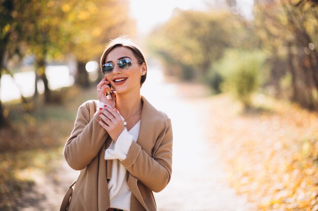 Mujer joven en el parque del otoño usando el teléfono