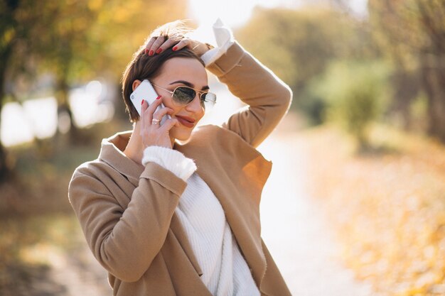 Mujer joven en el parque del otoño usando el teléfono