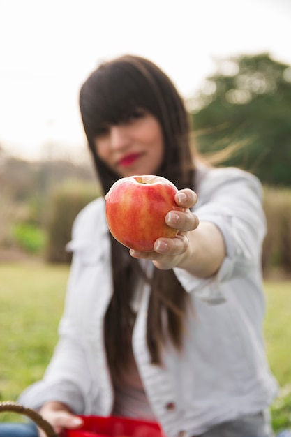 Mujer joven en el parque que muestra la manzana roja