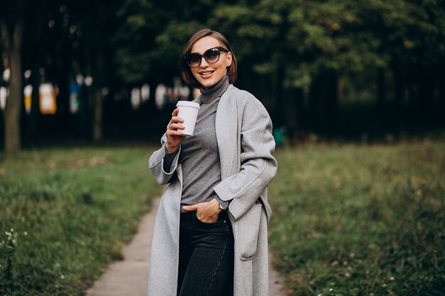 Mujer joven en el parque tomando café y hablando por teléfono