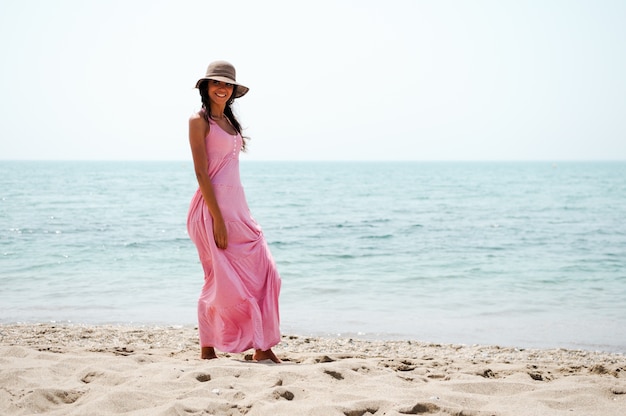 Mujer joven paseando por la playa con vestido rosa