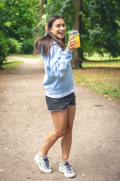 Una mujer joven en un paseo por el parque con jugo de naranja