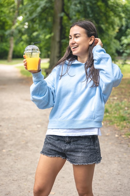 Una mujer joven en un paseo por el parque con jugo de naranja