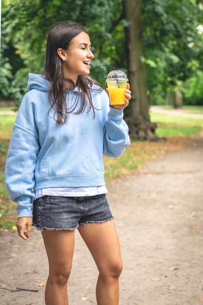 Una mujer joven en un paseo por el parque con jugo de naranja