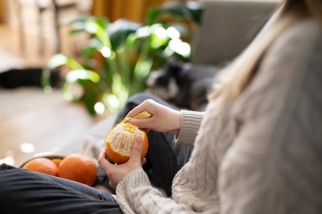 Mujer joven pelando una naranja en el sofá
